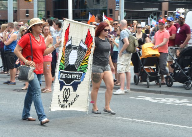 two women carrying a crocheted banner for Dykes on Bikes, walkers in a dyke march in Toronto 