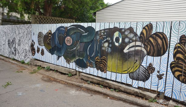 fish mural on a white wood fence, muted tones of greens, blues and browns. 