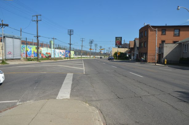 wide intersection where two roads meet in a V shape. not much else in the picture, only the nose of one car, no other traffic. hydro poles and wires in the picture