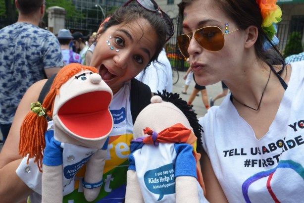 two young women with puppets, from the Kids Help Line float at the parade. One puppet is a girl and the other is a boy. 