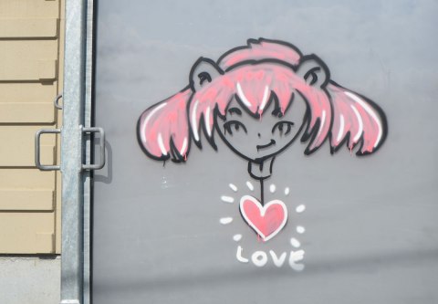 graffiti on a grey metal door of a girl's head with lots of pink hair. A pink heart beneath her with the word love under that