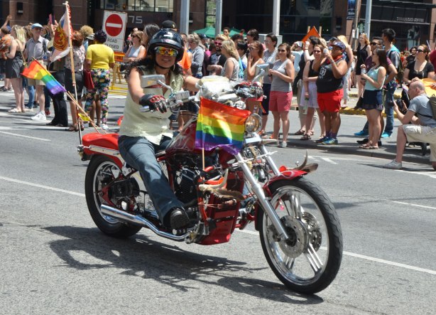 walkers in a dyke march in Toronto - a woman on a motorcycle with a rainbow flag