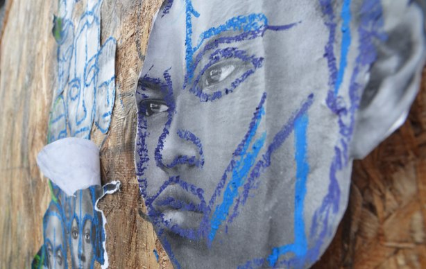 pictures of the faces of black men attached to wood construction hoardings and rough outlines and highlights drawn on the faces with crayon, in red, blue, yellow and green. 