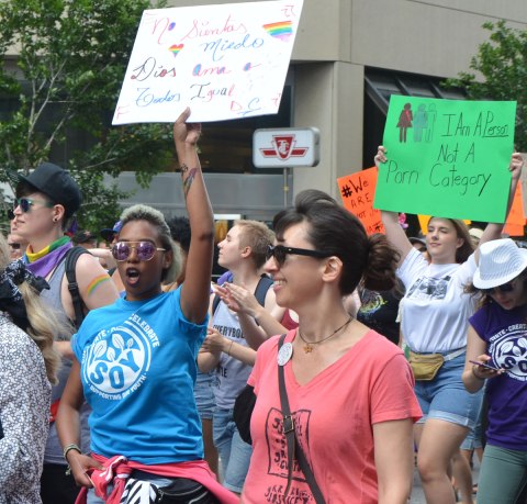 walkers in a dyke march in Toronto - a young black woman is shouting as she raises her sign in the air