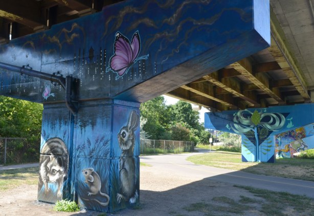 2 bents covered with murals. In the foreground, the mural is dark blue, with a pink butterfly, a rabbit, a mouse and a raccoon. 