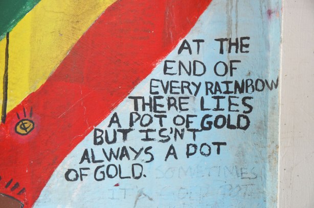 words written in black beside a red and yellow stripe, At the end of every rainbow there lies a pot of gold but isn't always a pot of gold. 