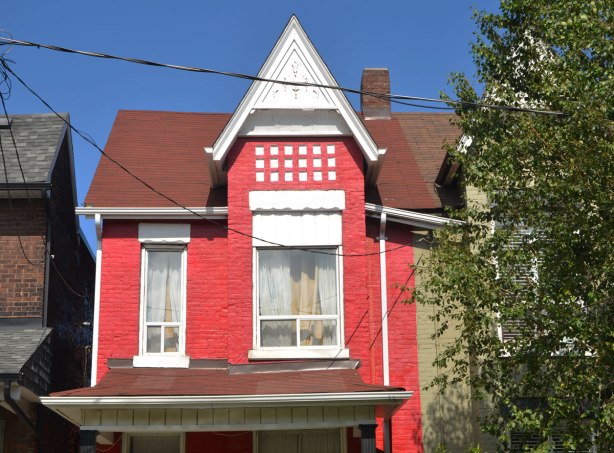 the top part of an old Victorian brick 2 storey house, painted red with white trim