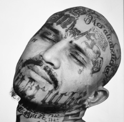 photo of a picture in a museum of a man's face that has been tattooed with gang symbols and words, 