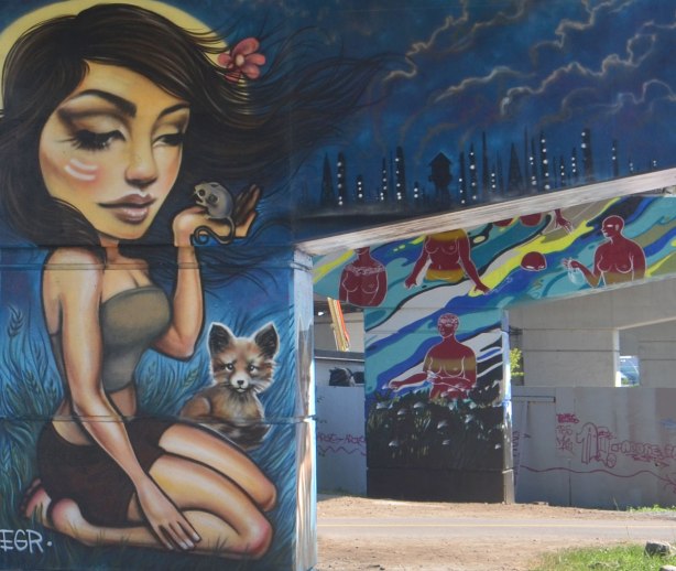 woman holding a mouse in a mural on a bent in the foreground, with another bent in the background, a mural of water and topless red women walking or standing in the water