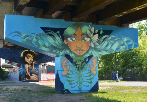 concrete support, or bent, under a ramp has been painted with a mural based on a woman's head coming through a large dark blue triangle