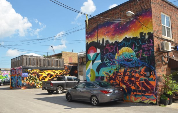 an alley with street art murals, a pickup truck and a car parked in front of one of the murals 