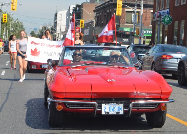 Two men in a red convertible sports car driving slowly down Woodbine Ave in a parade