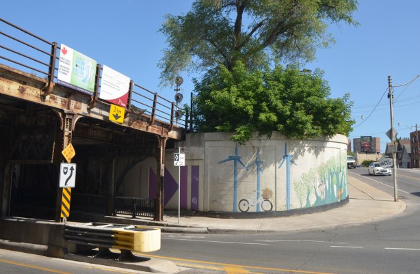 a wall of an underpass curves as it exits the railway bridge. on the curve is the continuation of a mural that was painted on the walls of the underpass. Windmills and bikes.