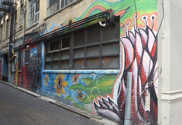 wall of an alley with a long window with worn painting around it of flowers and sunflowers