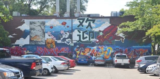 large mural across the side of a building at the back of a parking lot, Chinese characters and icons, panda bear, tiger, bamboo forest, lucky cat, chinese lantern, dragon