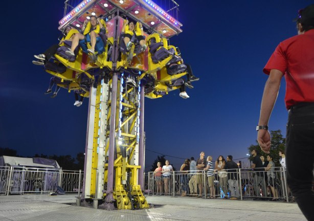 people wait in line for a ride that takes up up in the air and then drops you. A group has just begun their trip upwards. 