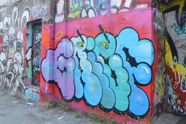 street art on a wall in an alley, text starting with G, two yellow eyes as well