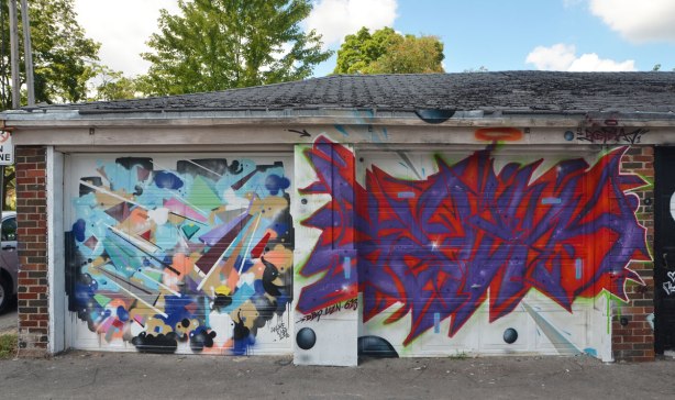 two garages in a lane with street art spray painted on their doors. 