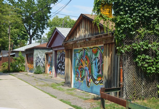three garages in an alley, each with street art painted on their doors. 