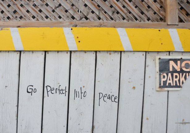 go perfect into peace, words written on a fence beside a no parking sign 