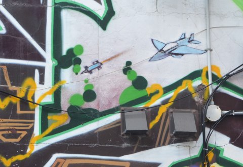 very small street art painting of a blue airplane amongst tags 