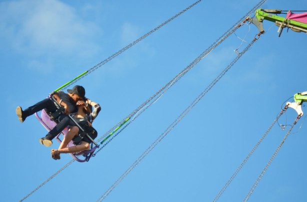 a young couple kissing on a swing that is up high
