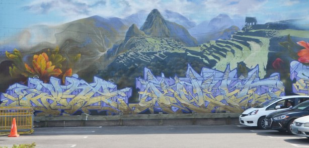 a mural with a panoramic scene of Machu Picchu, with graffiti writing signatues below. 
