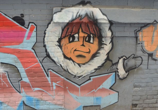 street art on a grey brick wall, head of a young man in a fur lined hood of a parka