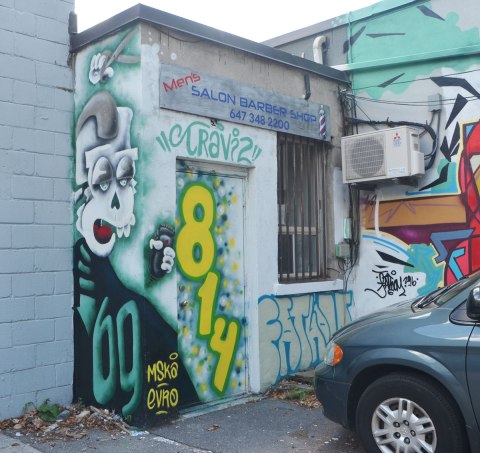 back door of men's hairsylist and barbershop, 814 Eglinton East with a white skulled creature holding a pair of scissors by mska as well as a large yellow 814 