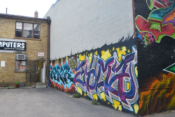 mural in an alley, horizontal street art aerosol spray paint artwork of text graffiti, two different ones side by side