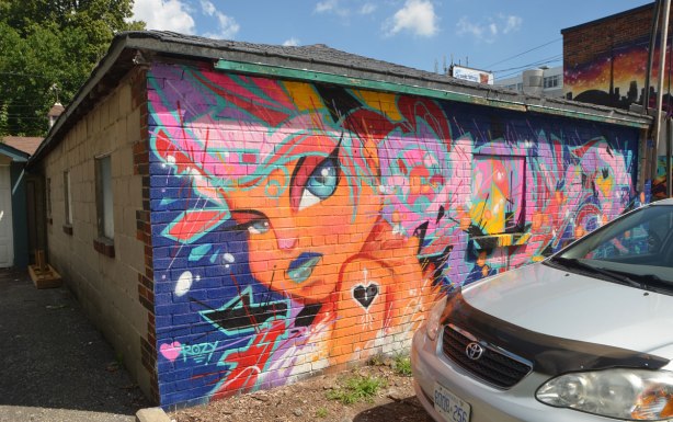 mural on the side of a garage by cruz 1 art, a young girl in orange with many colours abstractions around her