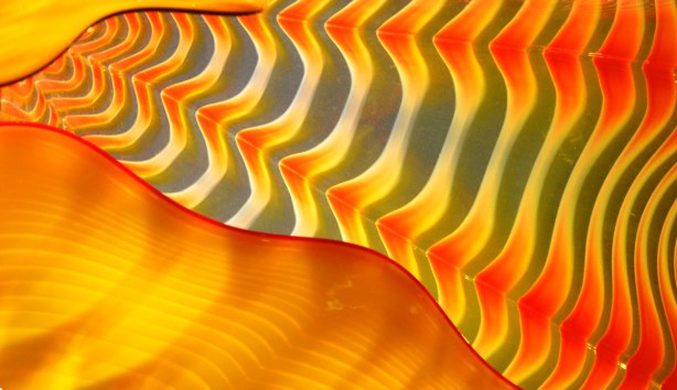 detail of a glass sculpture showing ripples and waves of colour, ornages, greys and yellows