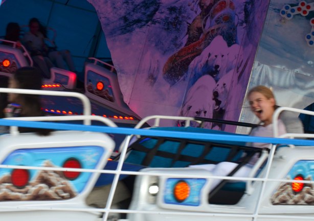 a young woman is screaming as a ride takes her around in circles, she is slightly blurry because of the speed of the ride 