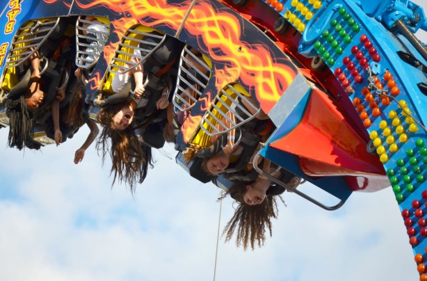 young women upside down on the Fire Ball midway ride, their long hair hanging down. 