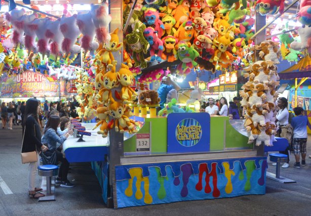 late evening on the midway at the Canadian National Exhibition, water game at the ex, piled high with stuffed prizes, and some people playing the game and some people watching the game 