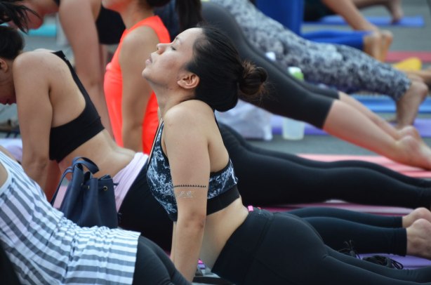 a woman with her eyes closed in the downward dog yoga position as she participates in a yogathon with many others, outside 