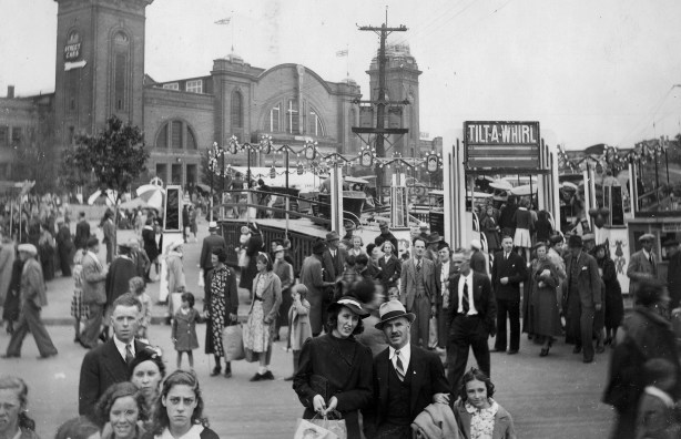 an old black and white photo of the midway at the CNE taken in 1937, lots of people in period clothes, an olf tilt-a-whirl ride also in the picture. 