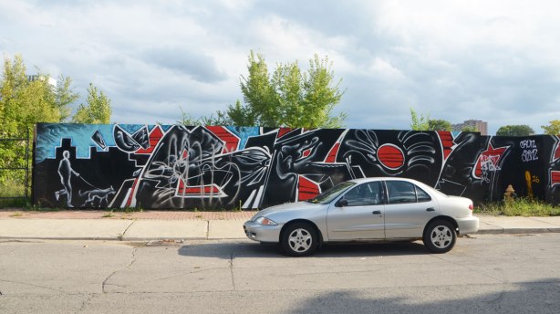 a car is parked in front of a mural painted on wood hoardings.