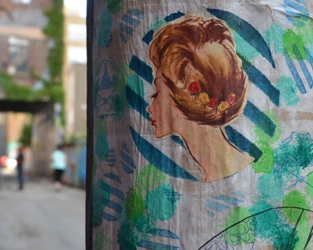 an old fashioned type drawing in colour of a woman's head, mostly only the back showing, some small flowers braided into her hair. 