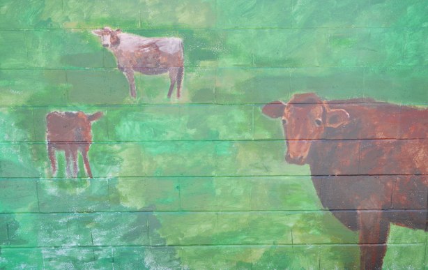 painting of three brown cows in a green field, painted on a garage door 