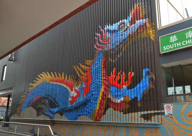 mural of a large blue dragon on a wall, outrside, with red and gold coloured spines