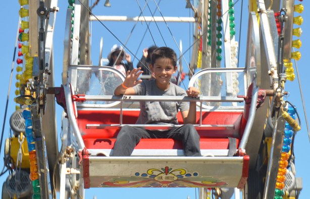 a boy is waving to the camera as he sits on a ferris wheel 