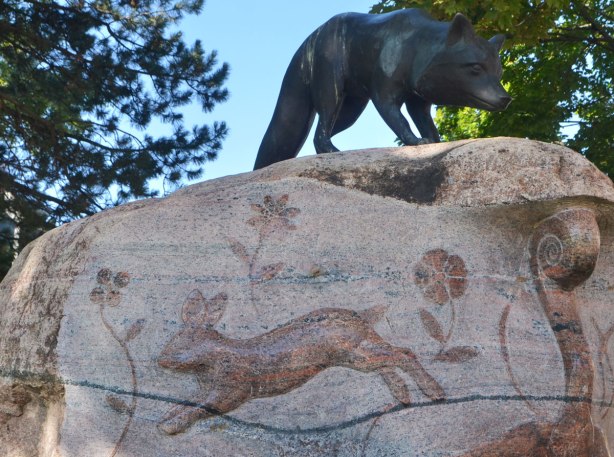 sculpture of a fox on top of a rocl. Carved into the rock is a relief picture of a rabbit and some flowers 
