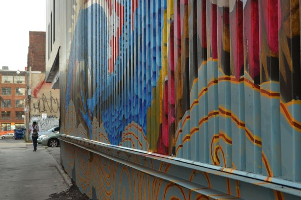 view down an alley, a mural is on the right, a girl is walking down the alley