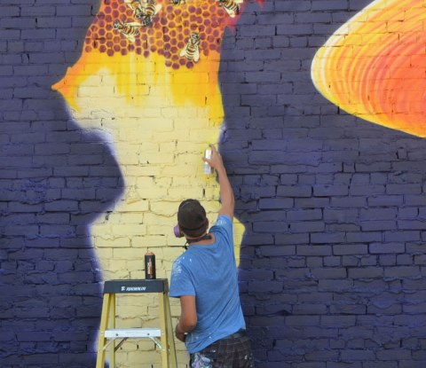 a man is painting a mural, this part is a honeycomb with some bees on it. Dark blue background. 