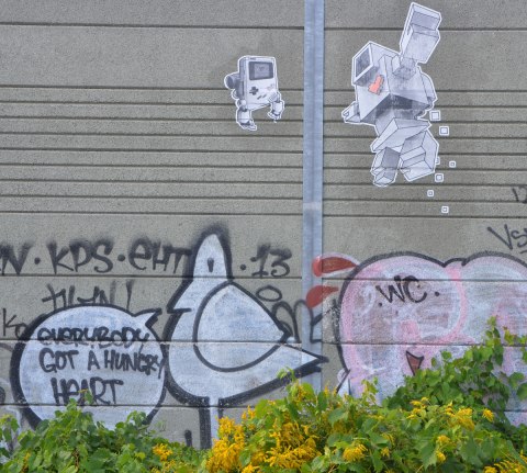 lovebot and a lovebot nintendo gameboy on a wall above a graffiti bird with a word bubble that says everybody got a hungry heart