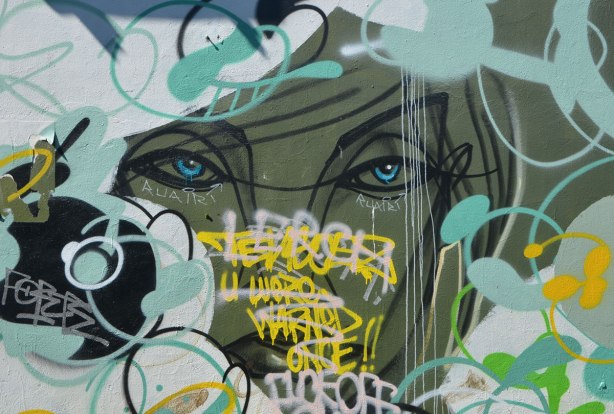 street art painting of part of a woman's face by anser, on olive green backgound, partially painted over and with words written in front of it. 