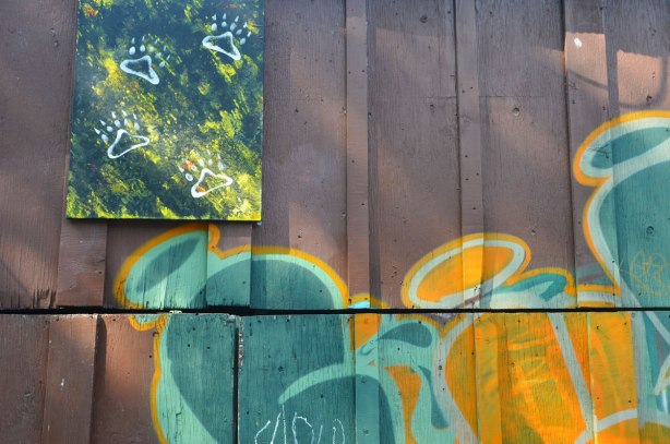 street art on a brown wood garage door, with a painting of white paw prints on blues and greens mounted near the top of the wall 
