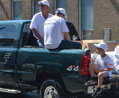 two men sitting in the back of a pick up truck as well as a boy sitting on the tailgate, in a parade, wearing white t-shirts that say Proud to be Union