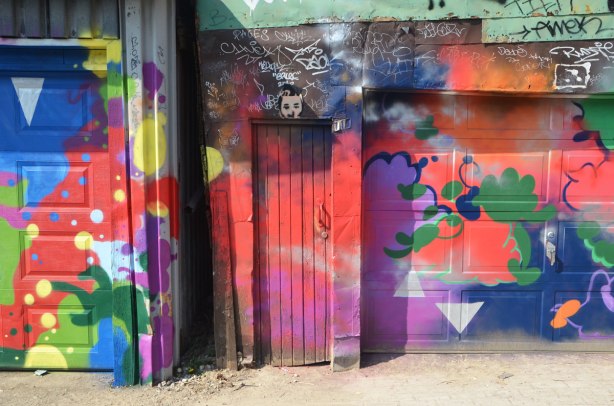 part of a garage door with a narrow wood door beside it, all covered with bright street art, abstract, mostly in red 